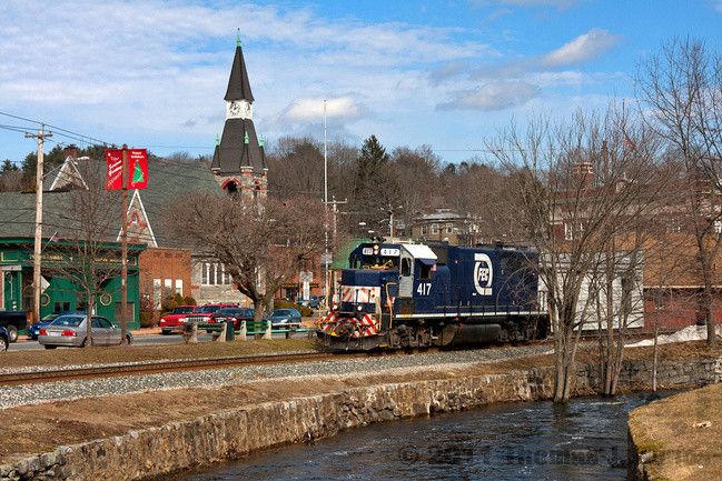 Scenic picture of Stafford Spring Connecticut with train, small river, and building pictured